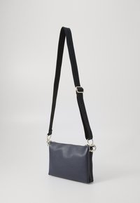 Marineblå lær crossbody-taske med glat overflade, slank rektangulær form, sølv hardware og en sort justerbar rem.