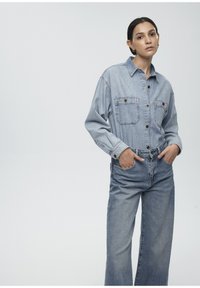 Light blue denim shirt with button-up front and two chest pockets, paired with loose-fitting light blue jeans. Smooth texture, casual design.