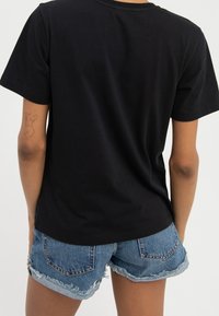 Czarny bawełniany t-shirt z okrągłym dekoltem i krótkimi rękawami, w połączeniu z przetartymi szortami dżinsowymi z postrzępionym dołem i tylnymi kieszeniami.