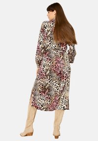 Abito animalier con diverse tonalità di rosa, marrone e crema; maniche lunghe; vita con cintura; fessure laterali; abbinato a stivali beige al ginocchio.