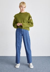 Grön ribbad stickad tröja med urklippta ärmar, parat med blå mönstrade vida byxor. Vita sneakers fulländar outfiten.