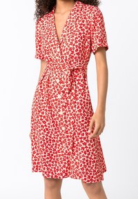 Czerwona i biała sukienka w kwiaty z krótkimi rękawami, zapięciem na guziki z przodu i wiązanym pasem. Lekki materiał, luźny krój i długość do kolan.