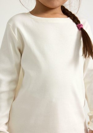 Hvid ribbet langærmet skjorte med rund halsudskæring. Blød tekstur og afslappet pasform, med en fletning holdt sammen af en lyserød hårelastik.