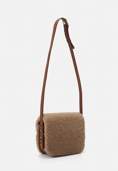 Brun shearling tvärs över kroppen-väska med kvadratisk form, läderrem, detaljer i guld och en mjuk texturerad yta. Justerbar remlängd.