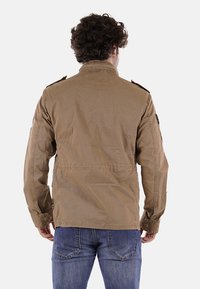 Giacca militare color beige con una vestibilità strutturata, spalline sulle spalle e tessuto strutturato. Presenta due tasche laterali e un colletto liscio.
