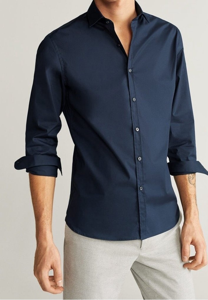 Camicia a maniche lunghe blu navy con colletto abbottonato, caratterizzata da una texture liscia e polsini arrotolabili, abbinata a pantaloni grigio chiaro.