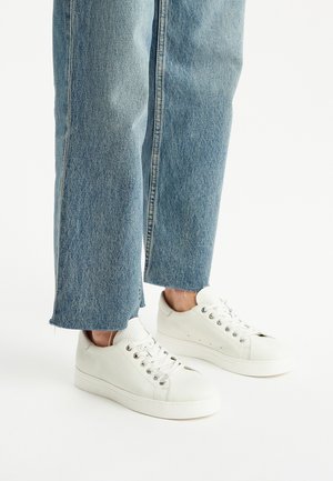 Witte leren sneakers met een gestructureerd oppervlak, voorzien van een ronde neus, metalen veterogen en een minimalistisch ontwerp, gecombineerd met lichtblauwe jeans.