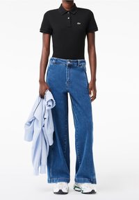 Polo noir avec un logo vert, sweat-shirt oversize bleu clair, jeans bleu large et baskets blanches avec des accents multicolores.