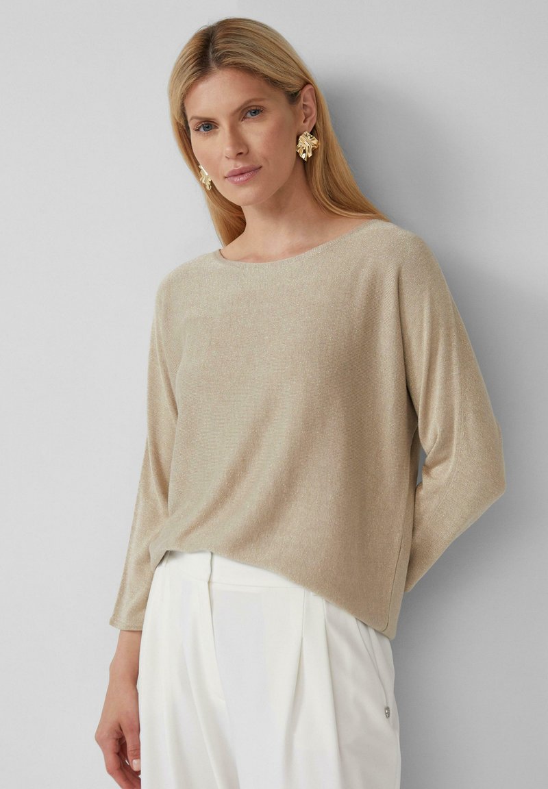 Beige, strukturiertes Langarmoberteil mit Bootshals, kombiniert mit weißen, plissierten Hosen. Verfügt über einen dezenten Glanz und einen lässigen Schnitt.
