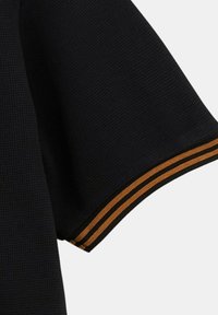 Manche en tissu noir texturé avec deux bandes orange parallèles près du bord sur un fond blanc.