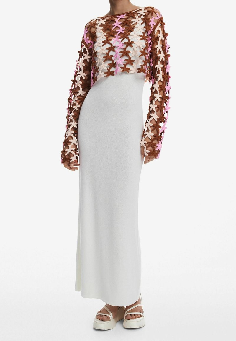 Hæklet sweater med brune, lyserøde og beige blomster mønstre; tætsiddende hvid kjole; modellen har platform sandaler på; glat tekstur, lange ærmer.