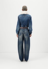 Chaqueta de mezclilla con cuello de piel sintética, diseño corto y puños elásticos, combinada con vaqueros azul claro de cintura alta y corte holgado.