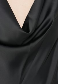 O tecido de satin preto cai em um decote em V, exibindo uma textura suave e lustrosa com dobras suaves e um brilho sutil.