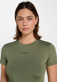 Olivgrünes, eng anliegendes T-Shirt mit kurzen Ärmeln aus glattem Material. Auf der Vorderseite ist ein dezentes "hummel"-Logo aufgedruckt.
