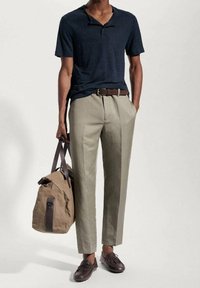 Granatowa koszulka polo z krótkim rękawem, jasnobeżowe dopasowane spodnie, brązowy pasek, brązowe skórzane buty i beżowa płócienna torba sportowa.