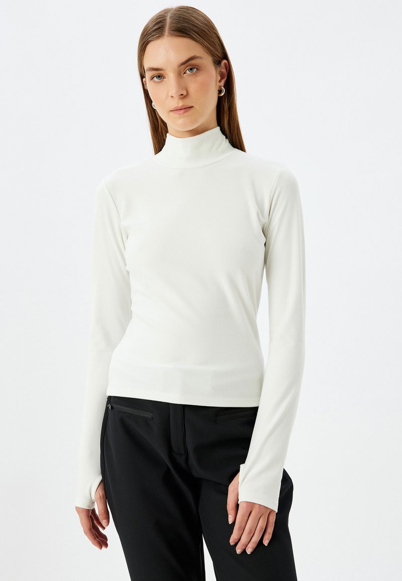 Witte turtleneck met lange mouwen, gemaakt van rekbare stof, met een slim fit en duimgaten bij de manchetten, gecombineerd met zwarte broek.