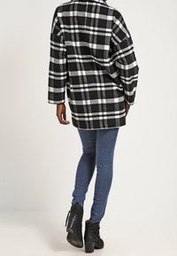 Giacca oversize a quadri bianco e nero con maniche lunghe, abbinata a jeans aderenti blu e stivaletti neri alla caviglia, caratterizzata da una vestibilità comoda.