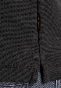 Zwarte polo met textuur, voorzien van een split-zoom en een PME Legend-label aan de zijkant. Zichtbaar stiksel en geweven patroon.