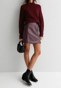 Burgundowy sweter z dzianiny, dopasowana spódnica z faux skóry w kolorze śliwkowym. Czarna torba typu bucket oraz botki na kostkę z grubym obcasem i metalicznymi akcentami.