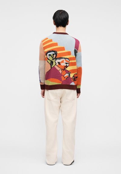 Πλεκτό πουλόβερ με πολύχρωμες αφηρημένες φιγούρες, με στρογγυλή λαιμόκοψη και ριμπ αξεσουάρ. Συνδυάζεται με χαλαρά παντελόνια σε εκρού απόχρωση.