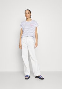 Striped short-sleeve t-shirt in light purple and white with a red flamingo design, paired with white wide-leg pants and blue sandals.