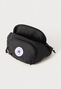 Borsetă neagră din material textil cu un design rotund, având un buzunar frontal cu fermoar și o appliqué circulară cu un logo, detaliat cu o stea albastră.