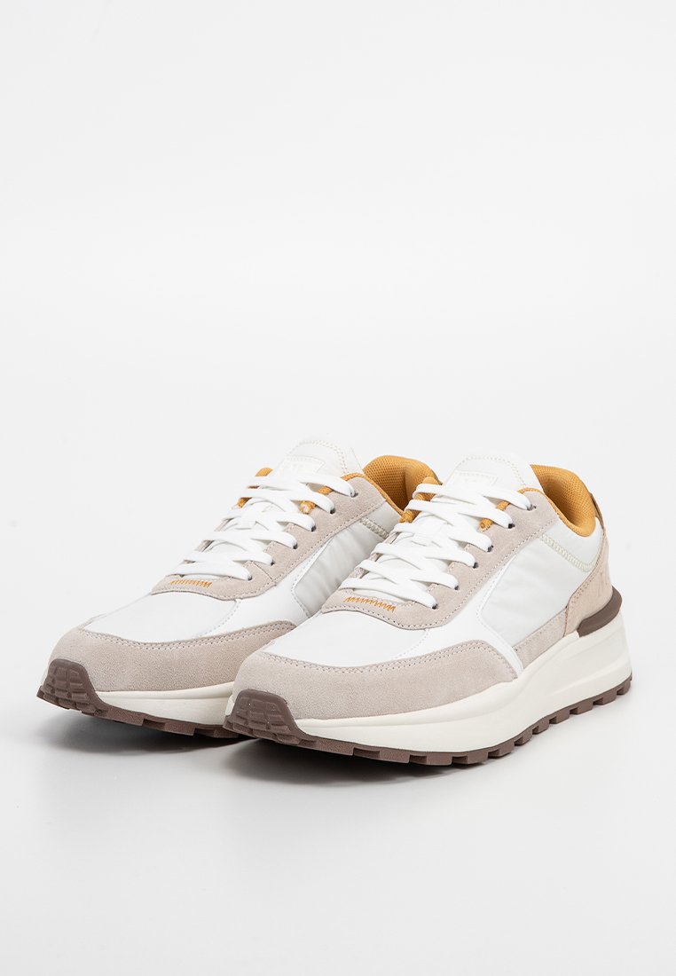 Ein Paar weiße und beige Low-Top-Sneaker mit weißen Schnürsenkeln, beigem Innenfutter und strukturierten braunen Gummisohlen auf einem weißen Hintergrund.
