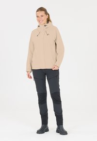 Ljusbeige vattentät jacka med justerbar huva, tillsammans med svarta byxor med blixtlåsfickor och kontrasterande paneler. Svarta stövlar ingår.