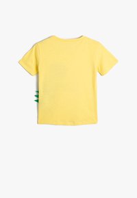 Gul kortærmet t-shirt med rund halsudskæring og grønne stofdetaljer på siden, der ligner pigge. Blødt bomuldsstof.