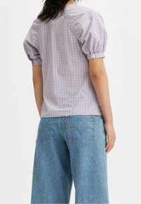 Blusa checkered viola con maniche a sbuffo, dettagli con bottoni sui polsini, abbinata a jeans a gamba larga blu chiaro con tasche posteriori classiche.