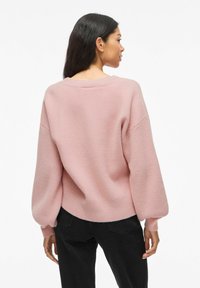 Overmaatse lichtroze sweater met een ronde halslijn en ballonmouwen, gemaakt van zachte, gestructureerde stof. De zoom is licht geribbeld.