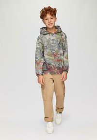 Hoodie met een multicolore abstracte patroon, grijze basis en een voorzak. Gecombineerd met beige cargobroek en witte sneakers.