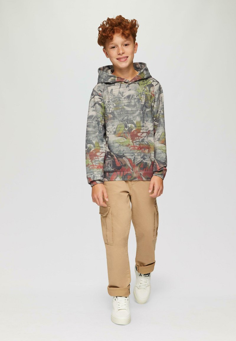 Hoodie met een multicolore abstracte patroon, grijze basis en een voorzak. Gecombineerd met beige cargobroek en witte sneakers.