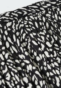 Černobílá skládající látka s abstraktním vzorem ve tvaru listu, lehká textura a hladký povrch, ideální pro oděvy.