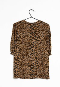 Haut en imprimé léopard marron et noir, en tissu doux, avec un col rond et des manches trois-quarts, suspendu à un crochet noir.