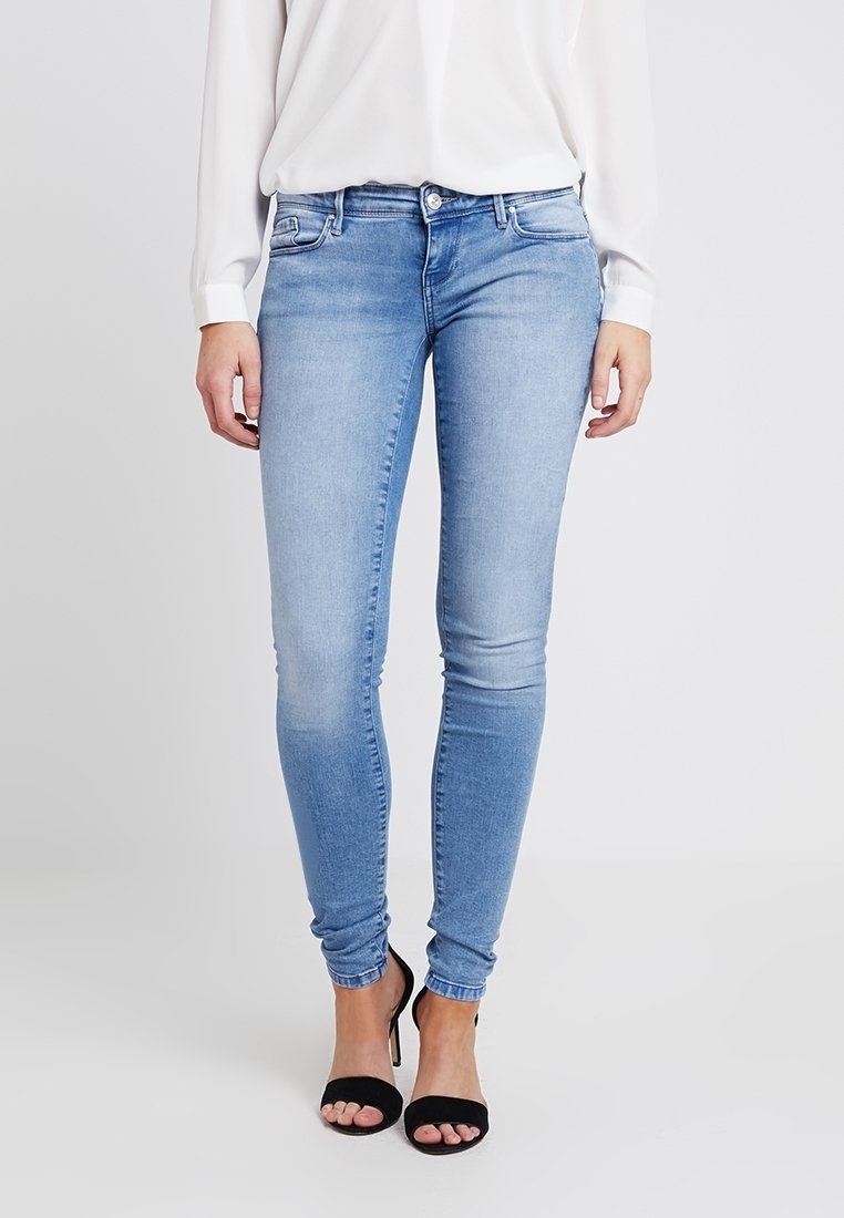 Vaqueros ajustados de un azul claro, confeccionados en denim, con un diseño clásico de cinco bolsillos y una textura suave. Llevados con sandalias negras.