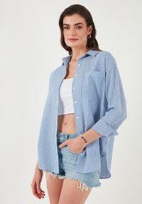 Light blue and white striped button-up shirt, long sleeves, chest pocket, relaxed fit, paired with denim shorts and a cropped top.