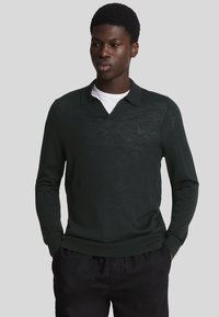 Dunkelgrüner langärmeliger Polo-Pullover mit V-Ausschnitt und einem dezenten Logo-Akzent. Hergestellt aus leichtem, strukturiertem Stoff.