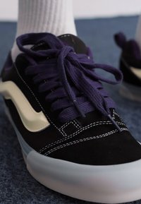 Baskets en daim noir avec des lacets violets, des coutures blanches et une bande latérale de couleur crème. Équipées d'une semelle en caoutchouc translucide.