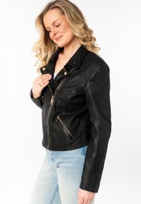 Zwart leren motorjack met ritszakken en een gesneden kraag. Heeft een getailleerd ontwerp en een gladde textuur.