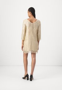 Beige blommönstrad klänning med broderi, trekvartslånga ärmar, rundad halsringning, textil med struktur och fålldetaljer, tillsammans med svarta klackskor.
