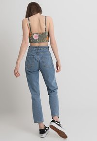 Floral crop top in groen en roze, met dunne bandjes, gecombineerd met lichtblauwe high-waisted jeans en zwarte sneakers met witte zolen.