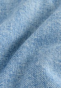 Tissu en denim bleu clair avec une texture lisse, présentant un motif de tissage classique. Le matériau montre une légère variation des teintes.