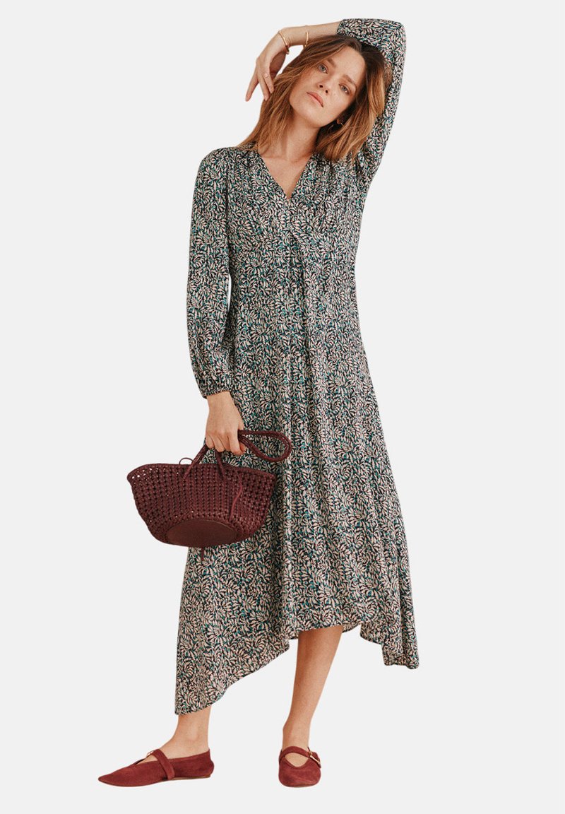 Blumenkleid mit langen Ärmeln, V-Ausschnitt, asymmetrischem Saum und einem Muster in Dunkelgrün, Pink und Weiß; kombiniert mit einer burgunderroten gewebten Handtasche und Schuhen.