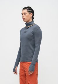 Top cinzento de manga comprida com gola alta, apresentando um detalhe multicolorido. Feito de um tecido suave com mangas ajustadas e aberturas para o polegar.