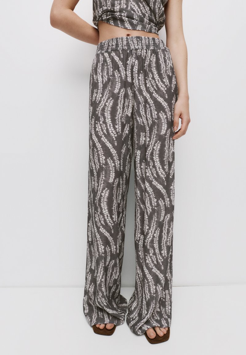Grijze gemusterde wijde broek met een elastische tailleband, voorzien van een golvend wit ontwerp en zachte textuur, gecombineerd met bruine plateau-schoenen.