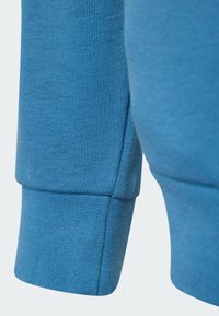 Blå sweatshirtstof med ribbet tekstur, der har en manchetærme og en ren finish. Materialet ser blødt og strækbart ud.