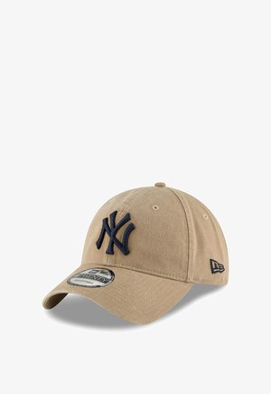 Bežs beisbola cepure ar tumši zilu izšūtu "NY" logotipu priekšpusē, izliekta mala un regulējama aizmugurējā siksna, lai pielāgotu izmēru.