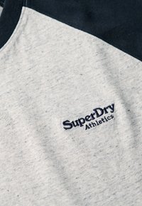 Hellgraues T-Shirt mit navyfarbenen Akzenten, aus Baumwolle, mit einer strukturierten Oberfläche und gesticktem "SuperDry Athletics"-Logo auf der Vorderseite.