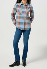 Rutigt långärmad skjorta i blått, rött och grönt. Har två bröstfickor, knappstängning fram och en spetsig krage. Bärs med slim jeans.